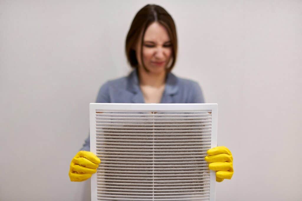 Woman holding dirty and dusty ventilation grille, disgusted